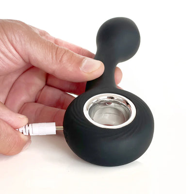 Hand holding a black silicone G-spot vibrator with a silver ring, shown being plugged in for USB charging.