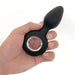 Hand holding a black rechargeable silicone anal plug with a circular metal ring handle against a white background.