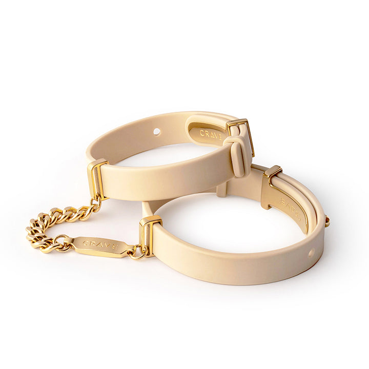 Beige silicone ID cuffs with 24kt gold-plated hardware and connecting chain, adjustable for wrist sizes 6.75 to 8.5 inches.