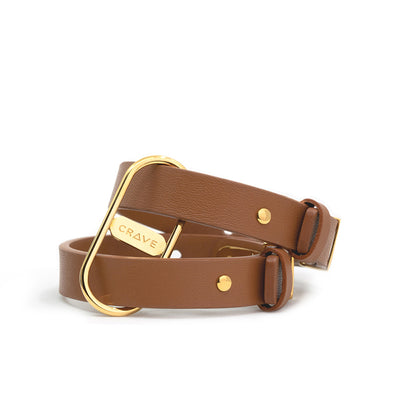 Tan genuine leather cuffs with 24kt gold polished hardware and Crave logo detail, adjustable for wrist sizes 6.75 to 8.5 inches.
