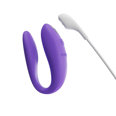 Purple We-Vibe Sync Go couples vibrator with white magnetic charging cable on white background.