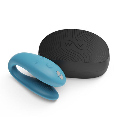 Blue We-Vibe Sync Go couples vibrator with ergonomic design next to a black textured travel case on white background.