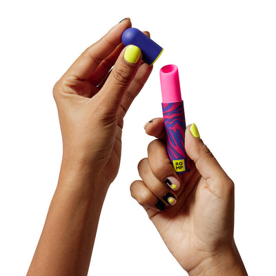 Hands holding a colorful ROMP Pleasure Air Lipstick clitoral stimulator with the cap removed, showing its pink silicone tip.