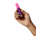Hand holding a compact ROMP Pleasure Air Lipstick stimulator with pink silicone tip and colorful patterned body.