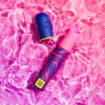 ROMP Pleasure Air Lipstick clitoral stimulator with colorful design and waterproof cap floating in pink water.