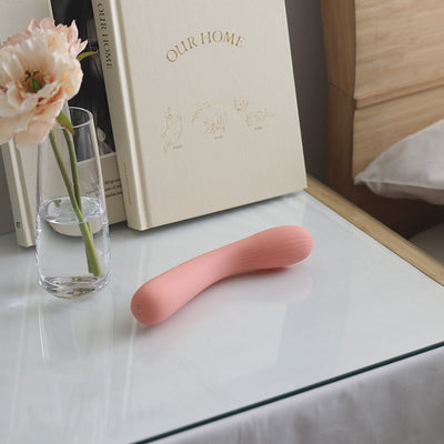iroha mai TOKI in soft pink placed on a glass bedside table next to a flower vase and books in a cozy bedroom setting