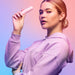 Woman in lavender hoodie holding a pink Vush Gloss Bullet Vibrator against a gradient pink and blue background