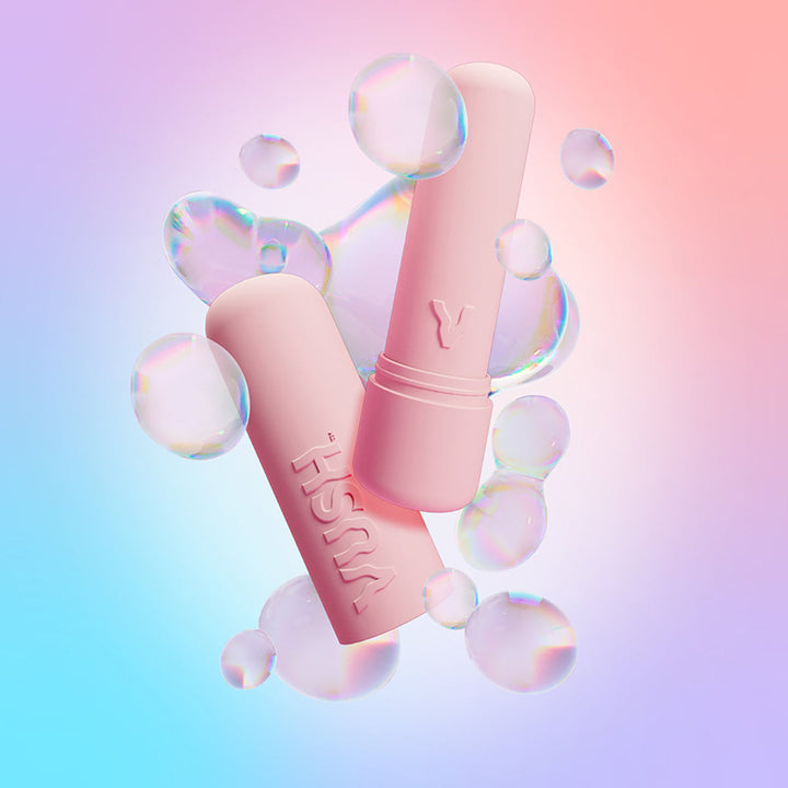 Pink Vush Gloss bullet vibrator with cap, surrounded by translucent bubbles on a pastel gradient background.