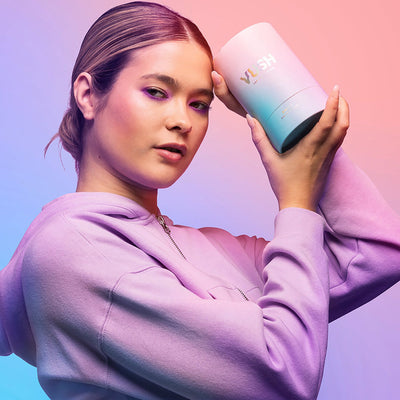 Woman in lavender hoodie holding a pastel gradient VUSH Swish Dual Tip Vibrator packaging against a pink and blue background