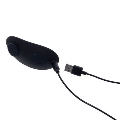 Black silicone remote control vibrator with USB charging cable attached on white background.