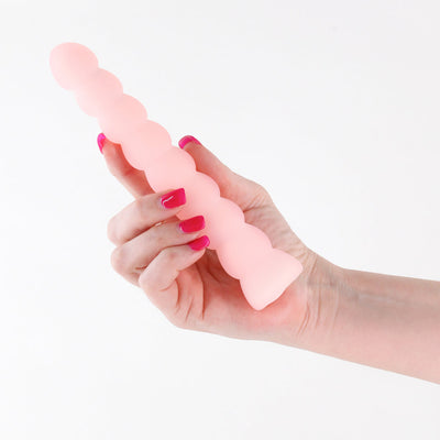 Hand holding a translucent peach-colored textured silicone vibrator with a beaded design against a white background.