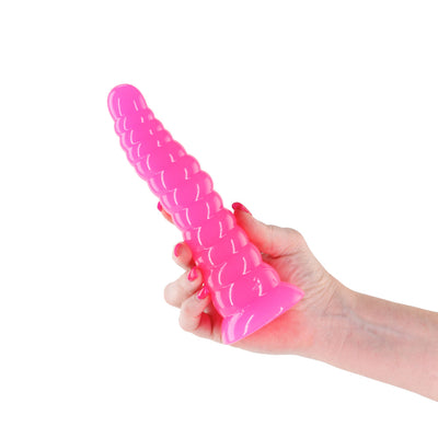 Hand holding a bright pink, textured glow-in-the-dark silicone dildo with a flared base against a white background.