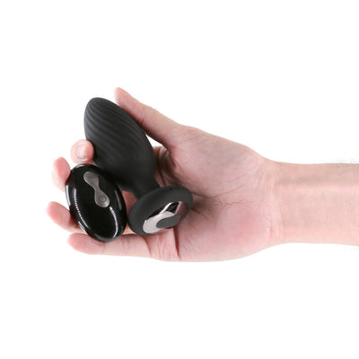 Hand holding a black silicone remote-controlled anal plug with textured surface and matching black remote.