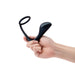 Hand holding a black silicone b-Vibe Ringer C-Ring with attached prostate plug against a white background.