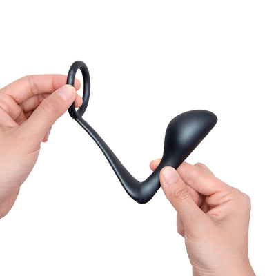 Hands holding a black flexible silicone b-Vibe Ringer C-Ring and prostate plug against a white background.