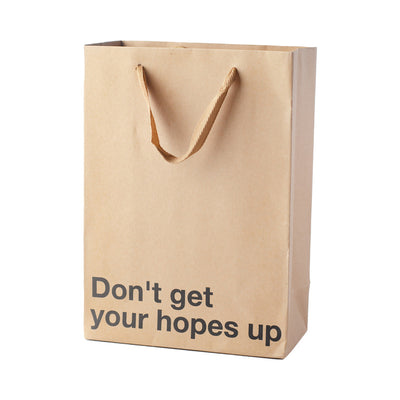 Kraft gift bag with brown ribbon handles and bold black text reading "Don't get your hopes up" on front
