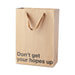 Kraft gift bag with brown ribbon handles and bold black text reading "Don't get your hopes up" on front