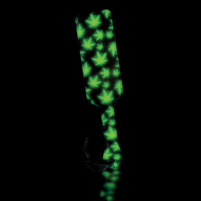 Glow-in-the-dark paddle with green cannabis leaf pattern and black wrist loop on a black background.
