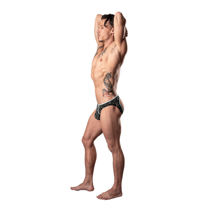 Fit male model wearing Male Power Marble Mesh Mini Moonshine jock in black with marble pattern and satin trim, posing with arms raised.
