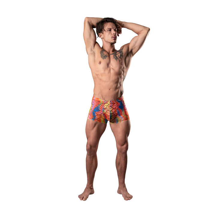 Athletic man wearing vibrant multicolor semi-sheer mesh pouch shorts with wavy lace pattern, posing with arms raised.