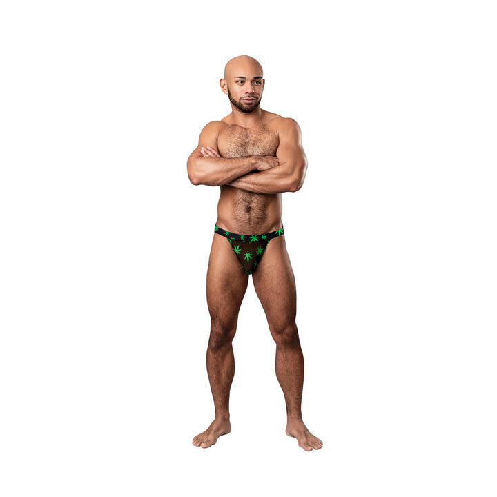 Man wearing Male Power Hazy Dayz black jockstrap with green pot leaf print standing with arms crossed