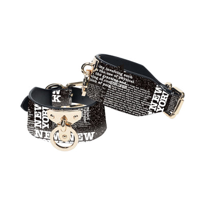 Black and white text print leg cuffs with gold-tone hardware and adjustable straps from the Ouch! NY Collection