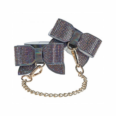 Iridescent bonded leather leg cuffs with bow design and gold chain connectors, adorned with sparkling rhinestones.