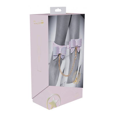 Packaging of Ouch! Paris Collection Leg Cuffs featuring iridescent bow ankle cuffs connected by a gold chain on a model's legs.