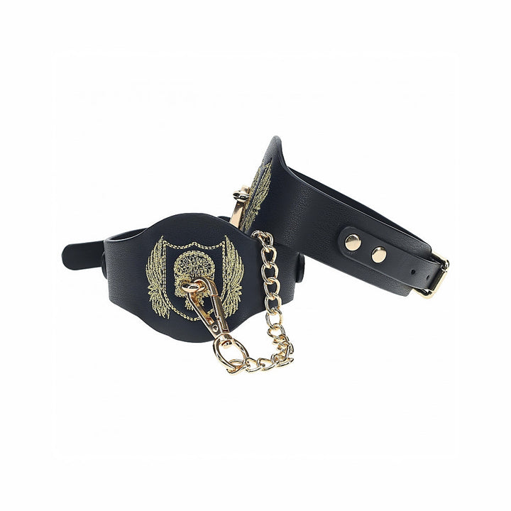 Black bonded leather leg cuffs with gold embroidered crest and iridescent gold chain and hardware details.
