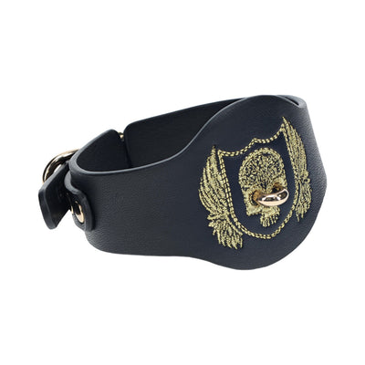 Black bonded leather leg cuff with gold embroidered skull and wings design and iridescent metal hardware.