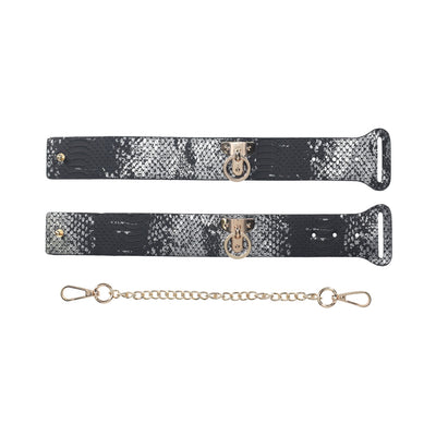 Pair of black and silver snakeskin-patterned leather handcuffs with gold-tone hardware and detachable gold chain restraint.