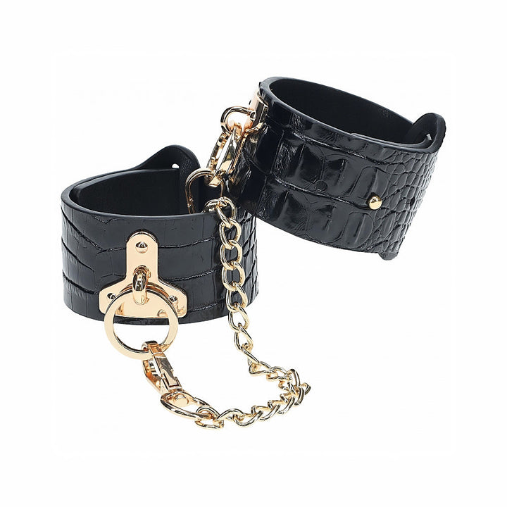 Black crocodile-textured leather handcuffs with gold-tone chain and hardware, featuring a secure and stylish design.