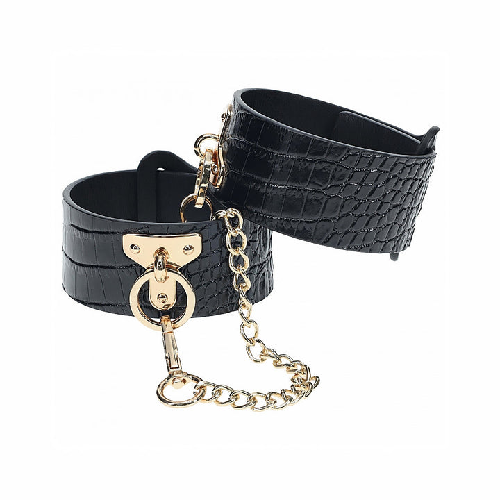 Black crocodile-texture leg cuffs with gold-tone chain and hardware detail on a white background.