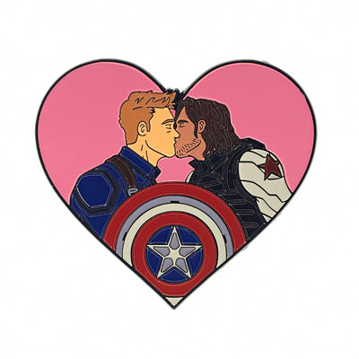 Heart-shaped enamel pin featuring two male characters in superhero costumes sharing a kiss with a shield emblem in front.