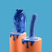 Blue speckled silicone dildo with suction cup base displayed on orange pedestal alongside matching velvet pouch and metal keychain accessory.