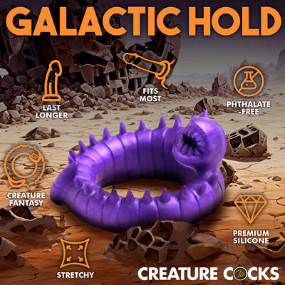 Purple silicone stretchy ring with spikes and a textured open mouth design, set against a desert fantasy background.