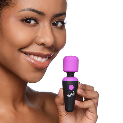 Smiling woman holding a compact black and purple BANG! 10X Vibrating Mini Wand with flexible neck against white background.
