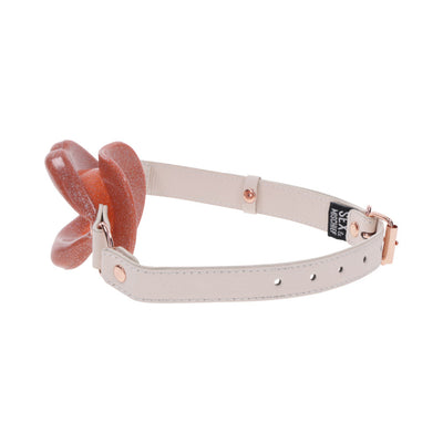 Peach pearlescent silicone lips gag with adjustable beige faux leather strap and rose gold buckle accents.