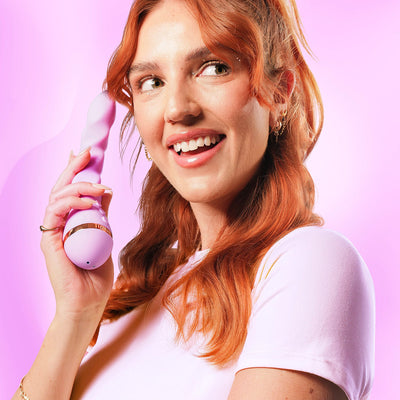 Smiling woman with red hair holding a lavender VUSH Siren Twist Vibrator against a pink background