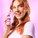 Smiling woman with red hair holding a lavender VUSH Siren Twist Vibrator against a pink background
