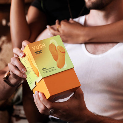 Person holding VUSH Luna Wearable Vibrator box with another person embracing them in the background.