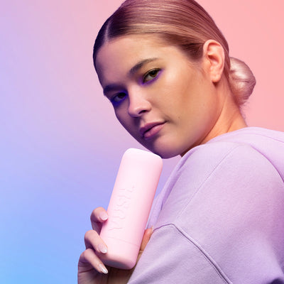 Woman in lavender hoodie holding a pink VUSH branded travel case against a pastel gradient background
