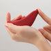Hand holding and gently pressing the smooth, curved red iroha+ TORI Renewal silicone personal massager.