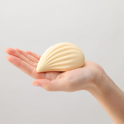 Hand holding a cream-colored, shell-shaped iroha+ KUSHI Renewal massager with soft ribbed texture.
