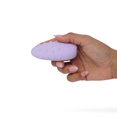 Hand holding a lilac double-sided clitoral vibrator with textured rounded dots on one side against a white background.