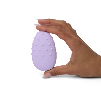 Hand holding a lilac Je Joue Mimi Deux double-sided clitoral vibrator with raised textured dots on one side.
