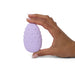 Hand holding a lilac Je Joue Mimi Deux double-sided clitoral vibrator with raised textured dots on one side.