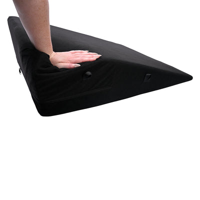 Black wedge-shaped foam positioner with a soft cover and integrated webbing loops, hand pressing down to show firmness.