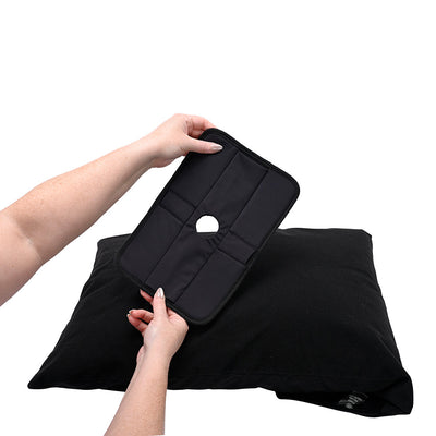 Hands holding the black Sportsheets Pivot Pillow Protector above a matching black pillow on a white background.
