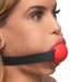 Close-up of a woman wearing a red silicone ball gag with an adjustable black locking strap.